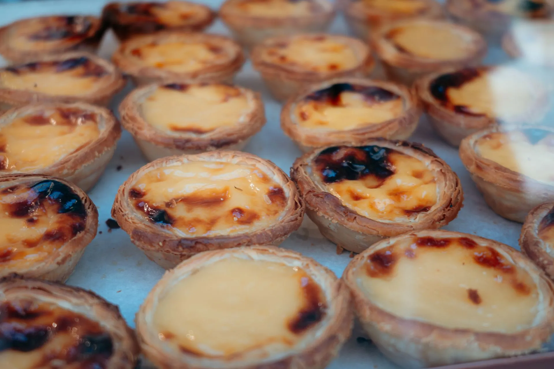 Hands shaping pastel de nata dough into tart tins on a floured kitchen counter in Lisbon