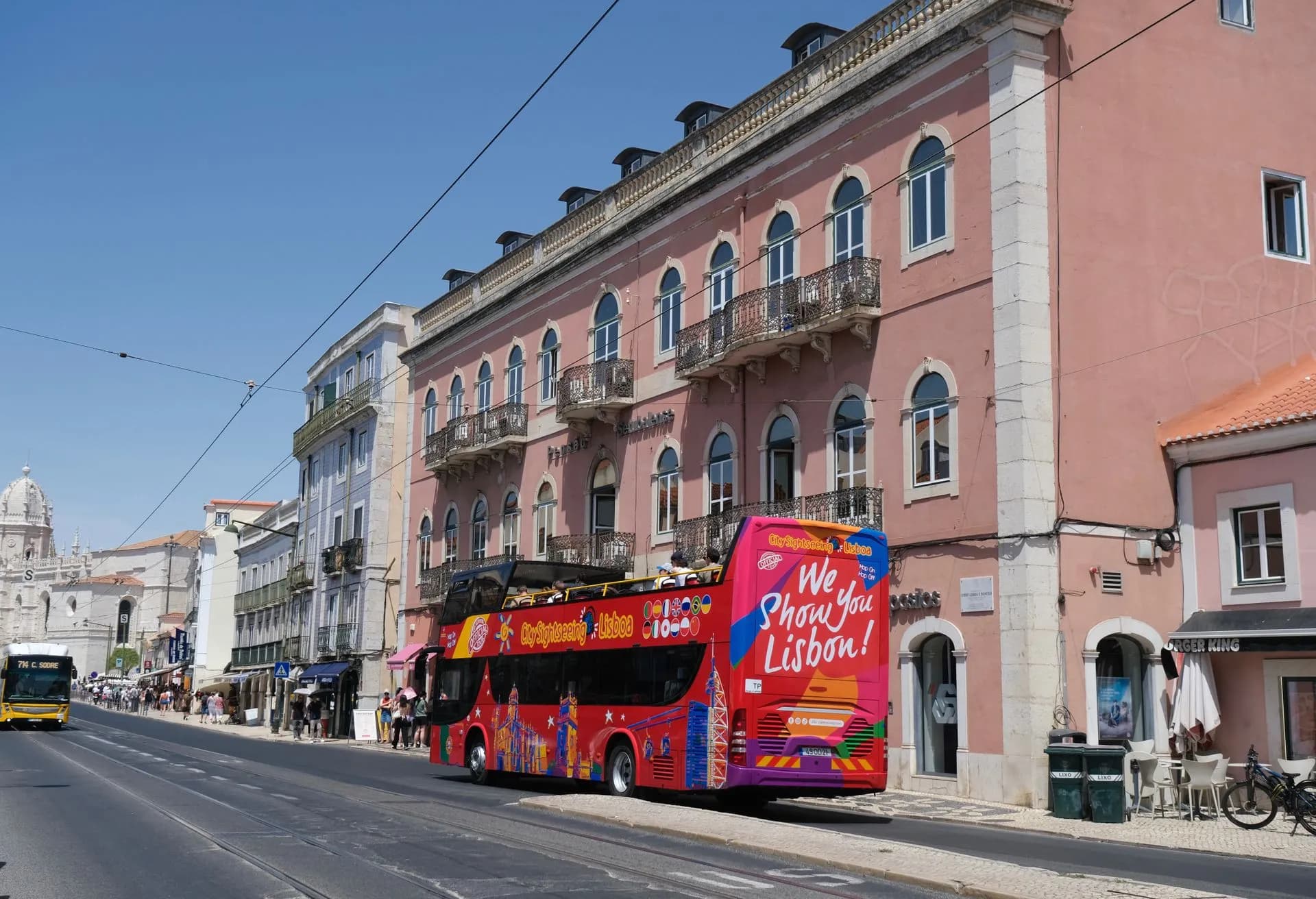 Open-top yellow double-decker sightseeing bus passing the Jerónimos Monastery in Belém, Lisbon