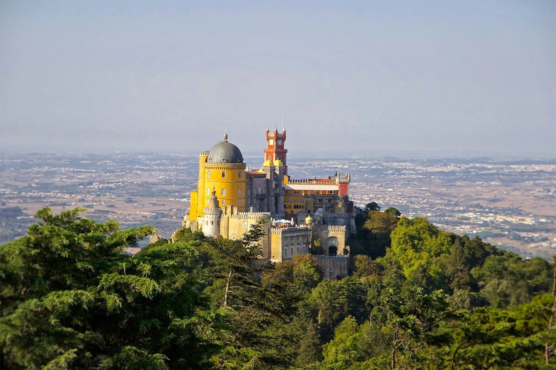 The red and yellow towers of Pena Palace rising above wooded hills in Sintra, Portugal