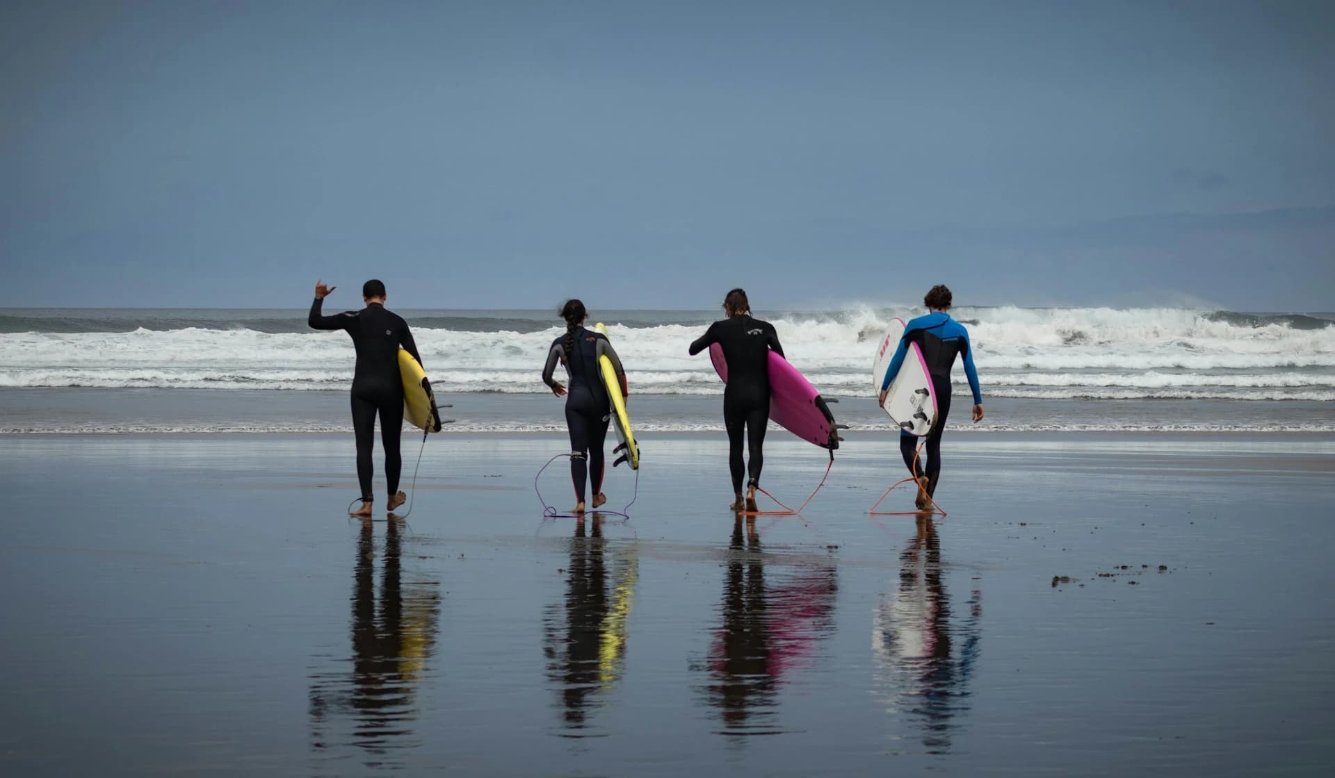 Beginner surfers carrying foam boards into the whitewater at a wide Atlantic beach near Lisbon