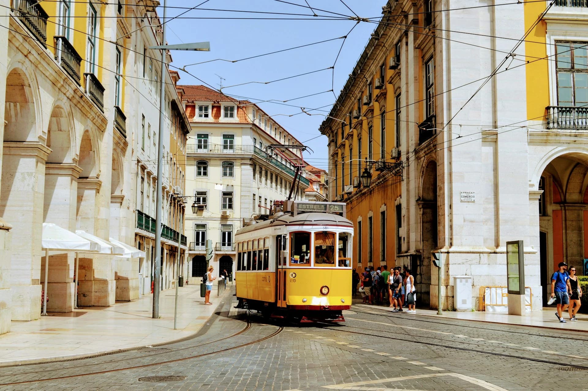 A yellow Remodelado tram climbing a narrow cobbled street between tiled buildings in Alfama, Lisbon