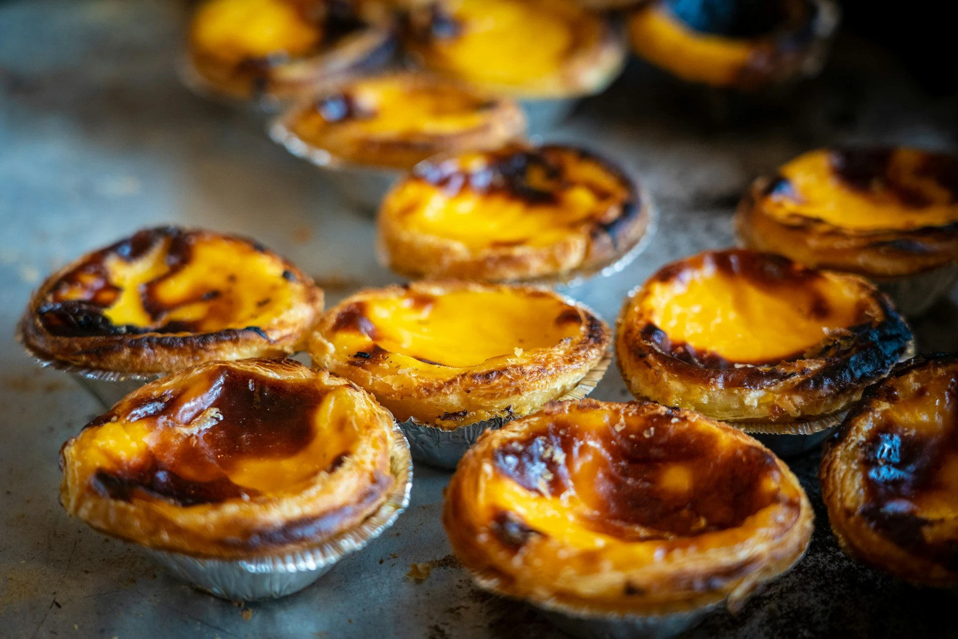 A tray of pastéis de nata fresh from the oven, their tops blistered and caramelised