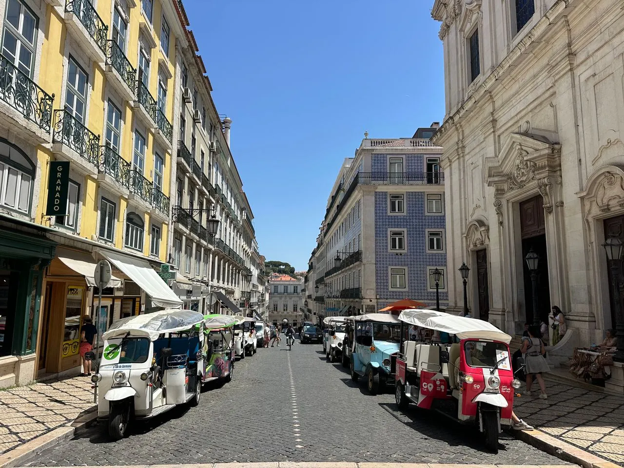 Tuk tuks lined up along a busy street in Lisbon